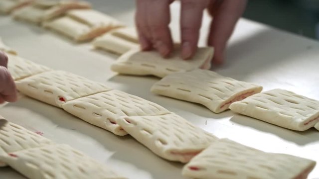 Close up hands of two unrecognizable factory workers turning over cookies moving along conveyor belt at confectionery