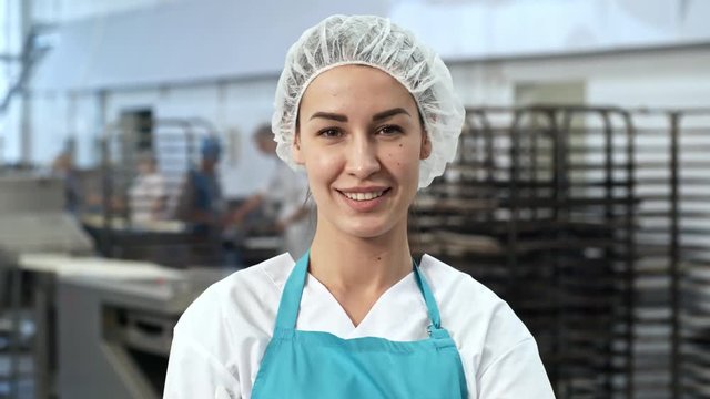 Tilt up shot of attractive young woman wearing bouffant mob cap and apron crossing arms and looking at camera