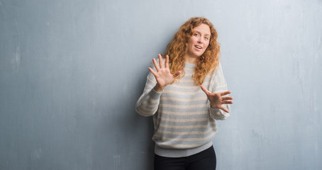 Fototapeta premium Young redhead woman over grey grunge wall afraid and terrified with fear expression stop gesture with hands, shouting in shock. Panic concept.