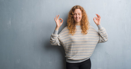 Young redhead woman over grey grunge wall relax and smiling with eyes closed doing meditation gesture with fingers. Yoga concept.