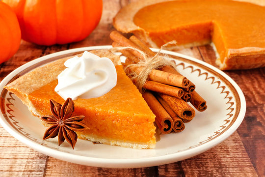 Slice of pumpkin pie with whipped cream. Close up scene on a rustic wood background.