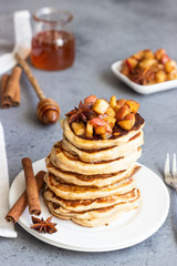 Stack of delicious sweet and spicy apple pancakes with fried caramelized apples, anise, cinnamon and honey on a white plate. Autumn breakfast. Copy space.