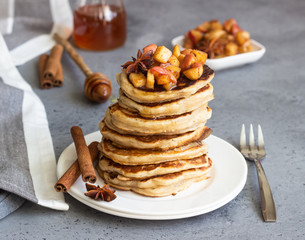 Stack of delicious sweet and spicy apple pancakes with fried caramelized apples, anise, cinnamon and honey on a white plate. Autumn breakfast. Copy space.