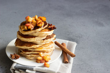 Stack of delicious sweet and spicy apple pancakes with fried caramelized apples, anise, cinnamon and honey on a white plate. Autumn breakfast. Copy space.