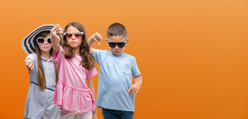 Group of boy and girls kids over orange background with angry face, negative sign showing dislike...