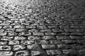 Black and white picture of a close-up of an old road with a texture of stone sun-drenched at sunset