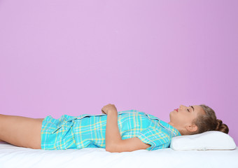Beautiful woman sleeping with orthopedic pillow on bed against color background
