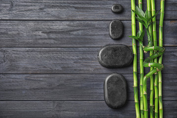 Obraz na płótnie Canvas Bamboo branches and spa stones on wooden background, top view. Space for text