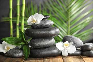 Spa stones with flowers on wooden table against blurred bamboo branches