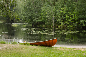 An orange boat with oars is on the shore of a forest lake. In the background there is a dense forest. Background.