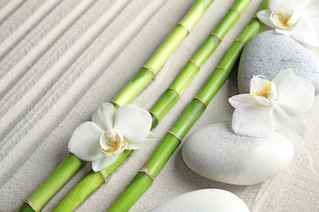 Bamboo branches with spa stones and orchid flowers on sand