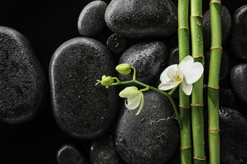 Fototapeta na wymiar Bamboo branches with spa stones and orchid on black background, top view