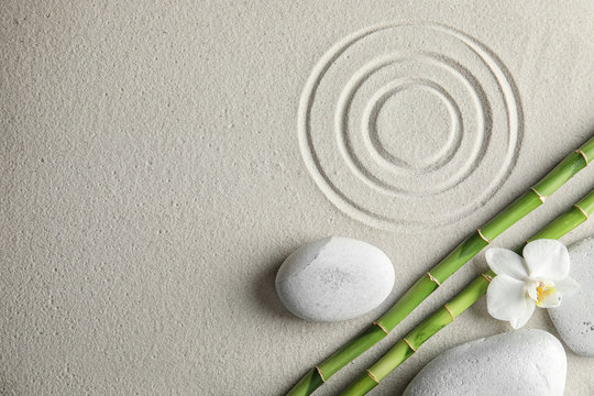 Bamboo branches with spa stones and orchid on sand, top view. Space for text