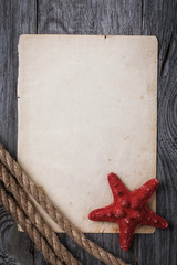 Old sheet of paper with rope and starfish on wooden board with copy space