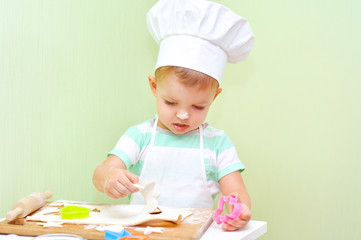 A little baker in a white suit chef bakes cookies from the dough