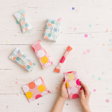 Top view on girl's hands with nicely wrapped Christmas or birthday gifts on white wooden table background. Holiday season.