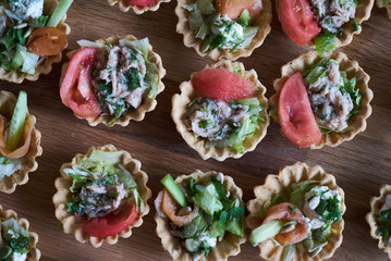 Tartlets with vegetables, chicken breast, cream and a slice of tomato on a wooden table.