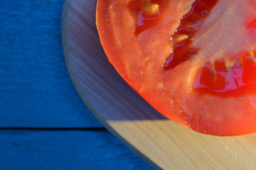 tomato slices are laid out on a wooden cutting board with blue-turquoise table illuminated by the sun with long cold shadow