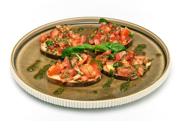 Traditional Italian appetizer,homemade bruscheta with tomatoes and basil served on brown plate, isolated on white background