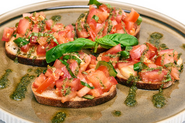 Traditional Italian appetizer,homemade bruscheta with tomatoes and basil served on brown plate, isolated on white background