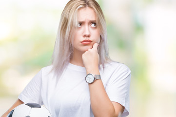 Young blonde woman holding soccer football ball over isolated background serious face thinking...