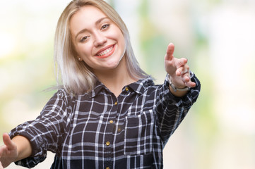 Young blonde woman over isolated background looking at the camera smiling with open arms for hug. Cheerful expression embracing happiness.