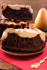 Cut pieces of chocolate dough pie with a curd layer, ripe pear on a red napkin.