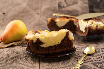 A sliced piece of cake on a round plate, a teaspoon, a ripe pear on a newspaper.