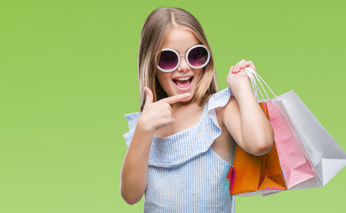 Young beautiful girl holding shopping bags on sales over isolated background very happy pointing...