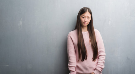 Young Chinese woman over grey wall with serious expression on face. Simple and natural looking at the camera.