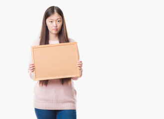 Fototapeta premium Young Chinese woman over isolated background holding corkboard with a confident expression on smart face thinking serious