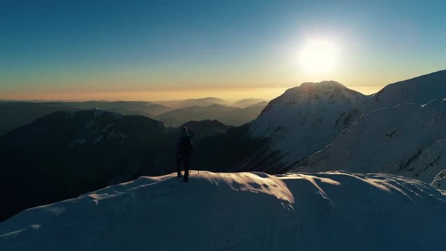 Aerial - Male mountaineer looking into the distance on top of snowy mountain