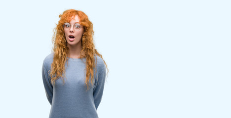 Young redhead woman wearing glasses scared in shock with a surprise face, afraid and excited with...