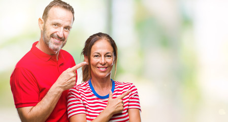 Middle age hispanic couple in love over isolated background cheerful with a smile of face pointing with hand and finger up to the side with happy and natural expression on face looking at the camera.