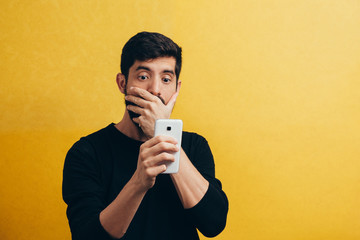 Shocked bearded man using mobile phone over yellow background