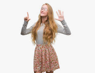 Blonde teenager woman wearing flowers skirt showing and pointing up with fingers number seven while smiling confident and happy.