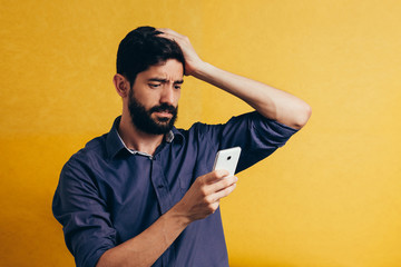 Shocked bearded man using mobile phone over yellow background