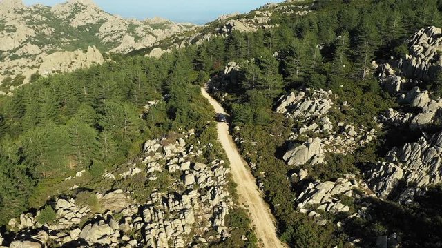 Video from above, aerial view of an off road car that is passing on a dirt road among the green mountains of Mount Limbara in Sardinia, Italy.