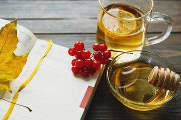 Tea and autumn coziness. A cup of tea, a book, maple leaves create an autumn mood  on a wooden background. cozy home