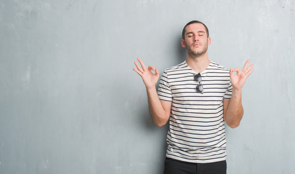 Young caucasian man over grey grunge wall relax and smiling with eyes closed doing meditation gesture with fingers. Yoga concept.