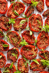 Dried tomatoes, dried tomato halves with the addition of aromatic herbs on a white wooden background, close-up