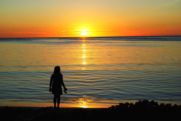 Fototapeta premium Silhouette of an unrecognizable woman watching the setting sun in Saipan, Northern Mariana Islands.