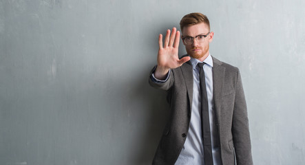 Young redhead elegant business man over grey grunge wall with open hand doing stop sign with serious and confident expression, defense gesture