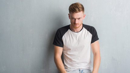 Young redhead man over grey grunge wall skeptic and nervous, frowning upset because of problem. Negative person.