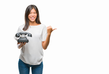 Young asian woman holding vintagera telephone over isolated background pointing and showing with thumb up to the side with happy face smiling