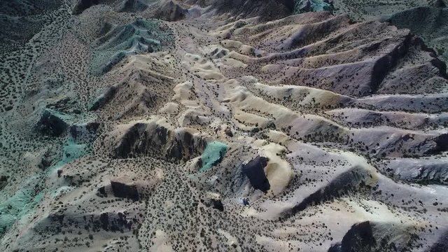 Aerial senital drone scene of colourfull sandy and rocky mountains. Blue, green, yellow, white, violet sand dunes with vegetation, eroded landscape in Uspallata, Mendoza, Argentina.