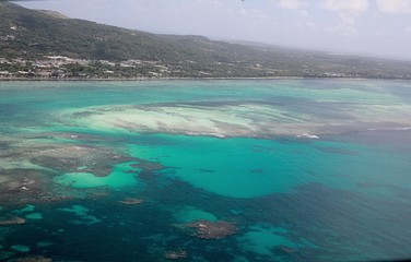 Saipan lagoon aerial view with its different shades of blue and green waters and the Beach Road in the distance