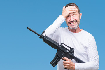 Middle age senior hoary criminal man holding gun weapon over isolated background stressed with hand on head, shocked with shame and surprise face, angry and frustrated. Fear and upset for mistake.