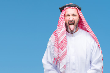 Senior arab man wearing keffiyeh over isolated background sticking tongue out happy with funny expression. Emotion concept.