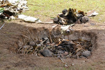 Traditional underground pit using heated stones and leaves and covered with earth to cook meat or...